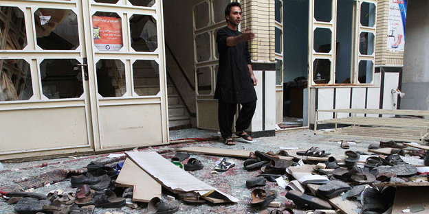 Ein Mann steht an der Tür zu einem beschädigten Gebäude, auf dem Boden vor ihm Schuhe und Bretter