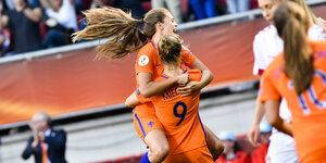 Zwei Frauen in orangefarbenen Fußballtrikots umarmen sich jubelnd