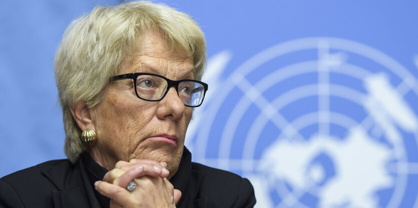 Carla Del Ponte hat das Kinn auf die verschränkten Hände gestützt und guckt durch ihre schwarz gerahmte Brille resigniert zur Seite