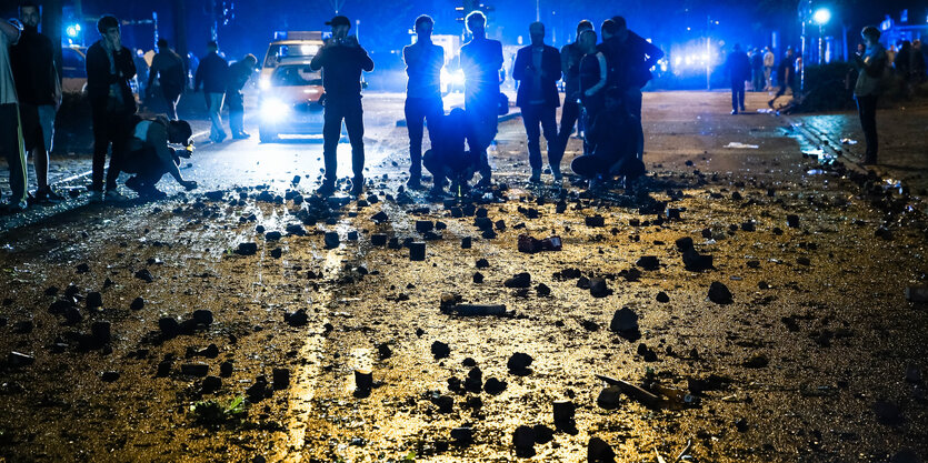 Menschen stehen vor einer Straße, die mit Steinen übersät ist