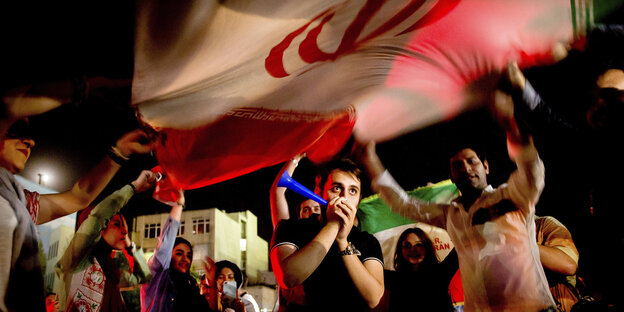 Iranische Fußballfans jubeln und schwenken eine Flagge