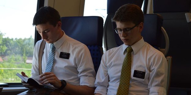 Zwei Männer in weißem Hemd sitzen im Zug