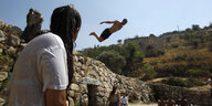 Männer stehen um eine antike Felsenmauer, von der gerade ein Mann springt