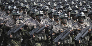 Nordkoreanische Soldaten mit schwarz getarnten Gesichtern marschieren mit schweren Waffen in Reih und Glied