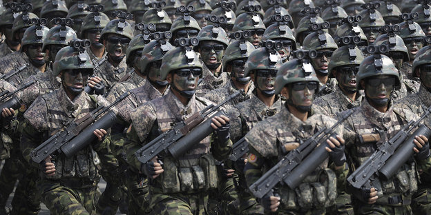 Nordkoreanische Soldaten mit schwarz getarnten Gesichtern marschieren mit schweren Waffen in Reih und Glied