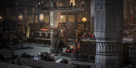 Schauspieler Idris Elba mit Pistolen bewaffnet in gotisch anmutendem Saal.