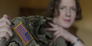 Eine Frau mit kurzen Haaren hält eine Militär-Jacke mit US-amerikanischer Flagge auf dem Arm hoch