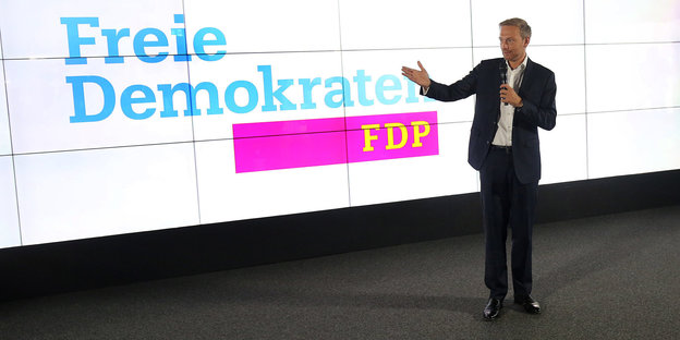 Christian Lindner zeigt auf das Logo von der FDP