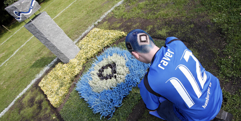 Ein HSV-Fan sitzt vor einem Grab mit HSV-Raute auf dem Altonaer Friedhof