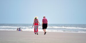 Ein älteres Paar spaziert am Strand entlang.