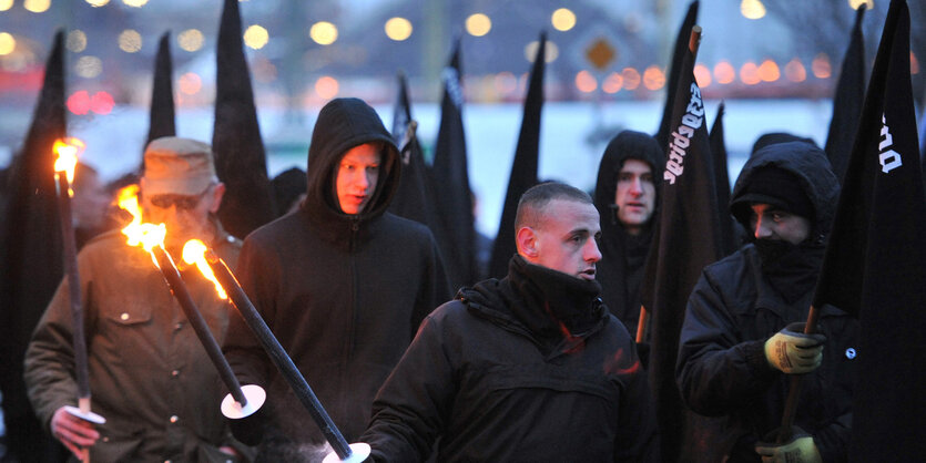 Neonazis stehen mit schwarzen Flaggen und Fackeln beieinander