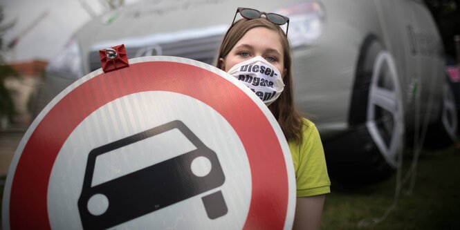 Eine Frau mit Mundschutz und einem Autoverbotsschild