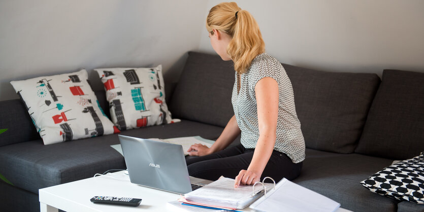 Eine Frau sitzt auf dem Sofa und arbeitet an einem Laptop.