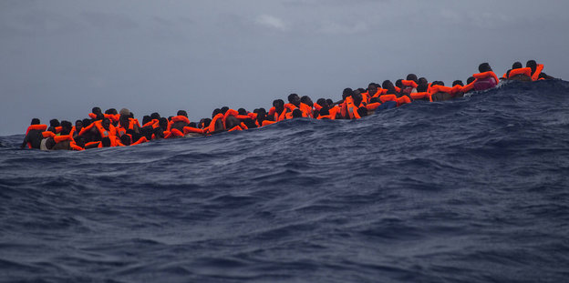 Migranten mit roten Schwimmwesten im Meer