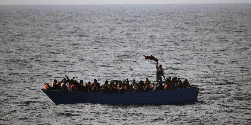 Ein Boot auf hoher See, darin viele Menschen mit Schwimmwesten