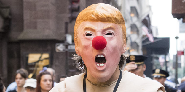 Ein Mensch trägt eine Maske mit einem verzerrten Gesicht des US-Präsidenten Donald Trump
