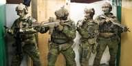 Vier Soldaten stehen in unterschiedlichen Posen mit ihren Waffen