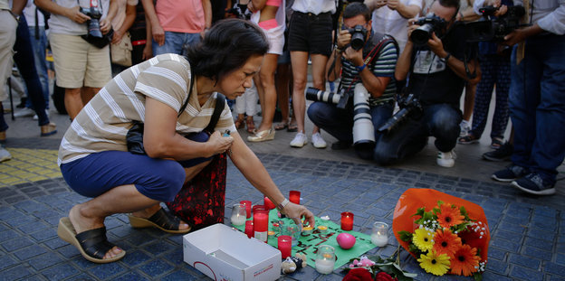 Eine Frau stellt eine Kerze auf ein Plakat an den Ramblas in Barcelona: „Catalunya – place of peace“