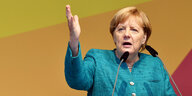 Angela Merkel auf einem Podium im Porträt, ihre rechte Hand zeigt in die Höhe