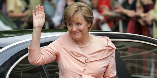 Angela Merkel steigt aus einem Auto und hebt den Arm zum Gruß