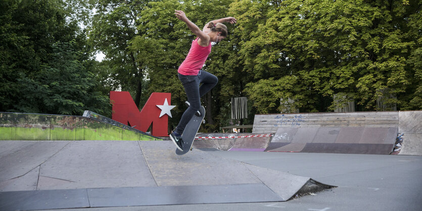 Eine junge sportliche Frau beim Sprung mit einem Skateboard über eine kleine Rampe