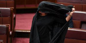 eine Frau zieht sich eine Burka vom Kopf