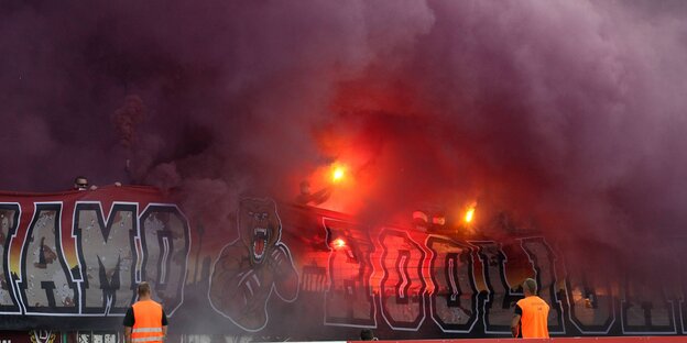 Orange-leuchtende Flammen inmitten von riesigen Rauchwolken auf einer Fußball-Tribüne