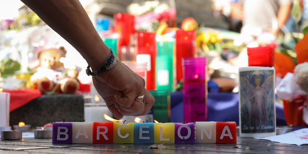 Hand zündet eine Kerze an, davor die Aufschrift "Barcelona"