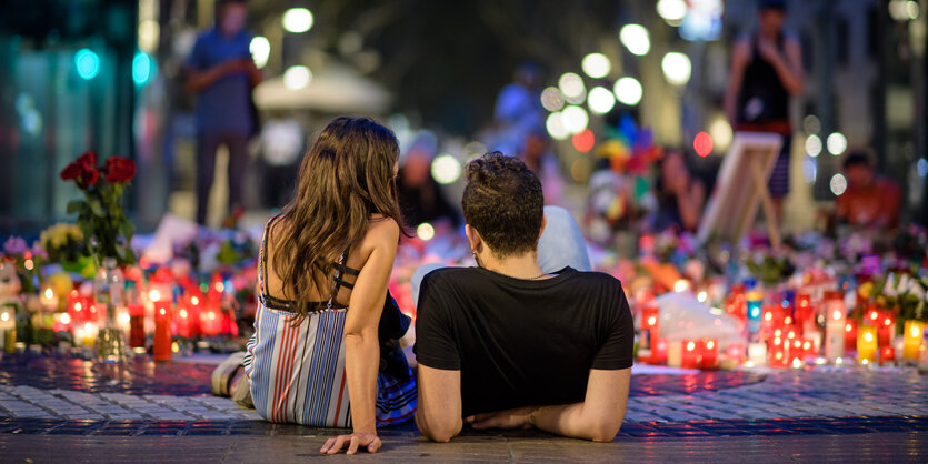 ZWei Menschen sitzen auf der Erde vor vielen Blumen und Kerzen