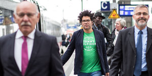 Ijoma Mangold geht in grünem T-Shirt und Jackett an einem Bahnsteig entlang