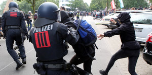 Ein Polizist hält einen Demonstranten am Arm fest und setzt seinen Schlagstock ein