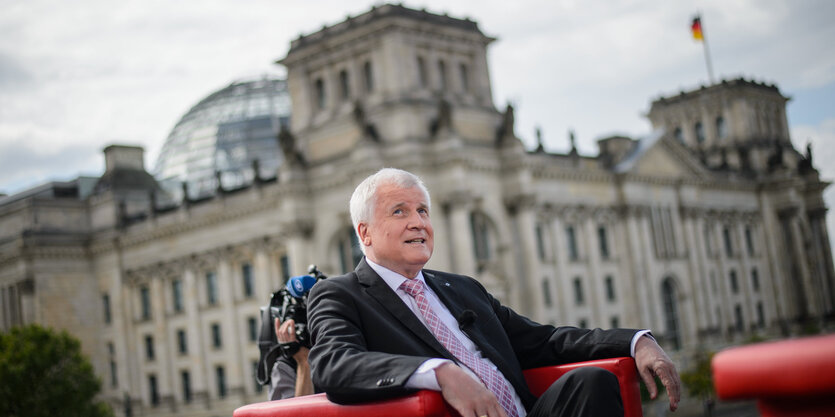 Horst Seehofer sitzt in einem roten Sessel, im Hintergrund der Berliner Reichstag