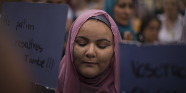 Eine Frau mit Kopftuch steht in einer Menschenmenge. Sie weint.
