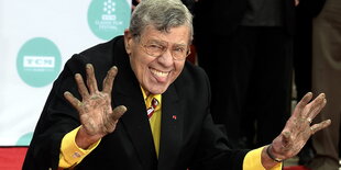 Jerry Lewis hebt seine schmutzigen Hände, lächelt und streckt dabei die Zungenspitze heraus