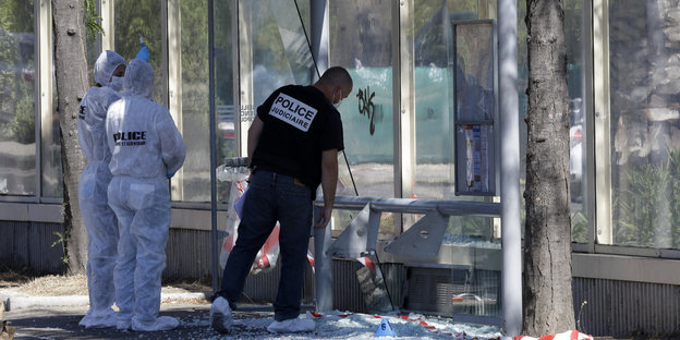 Personen mit dem Schriftzug "Police" auf dem Rücken in einer Bushaltestelle, deren Glaswände zersplittert sind