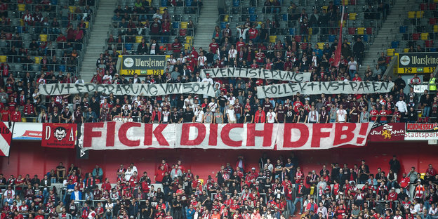 Fans halten in einem Fußballstadion Transparente mit der Aufschrift "Untergrabung von 50+1", "Eventisierung", "Kollektivstrafen" und "Fick dich DFB!" in die Höhe