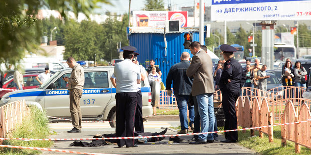Polizisten stehen am 19.08.2017 in Surgut (Russland) an dem Ort eines Messerangriffs neben einer auf dem Boden liegenden Person.