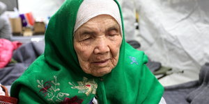 Eine alte Frau mit grünem Kopftuch sitzt in einer Notunterkunft