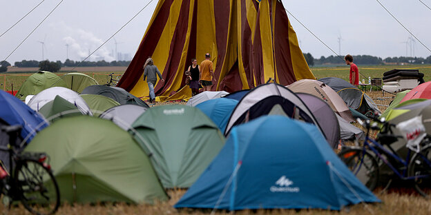 Einige Klimacamper stehen vor einem großen gelb-braun gestreiften Zelt, davor sind kleinere blaue, grüne und braune Zelte zu sehen