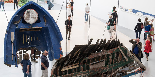 Teile eines zerbrochenen Bootes hängen in einer Ausstellungshalle