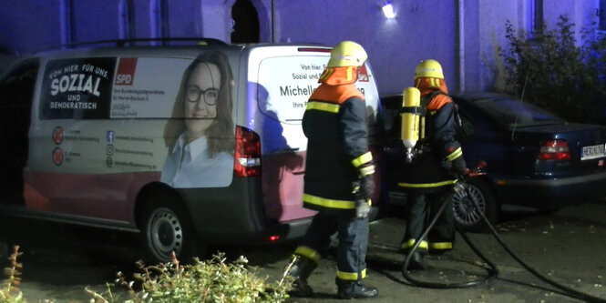 Feuerwehrleute laufen abends an einem Fahrzeug vorbei. Auf dem Auto: das Konterfei der Politikerin Michelle Müntefering