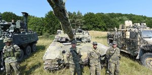 Soldaten stehen neben Panzern, das Panzerrohr ragt in die Kamera