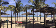 Touristen liegen am Strand unter Palmen, davor ein Gitterzaun
