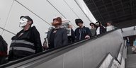 Menschen mit Masken fahren eine Rolltreppe herunter