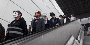 Menschen mit Masken fahren eine Rolltreppe herunter