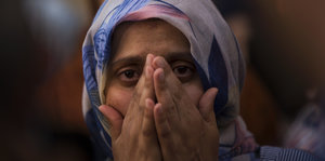 Eine Frau mit Kopftuch hält die Hände vor das Gesicht