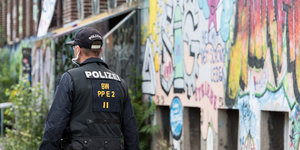 Ein Polizist in Montur läuft neben eine Hauswand, die mit Graffiti besprüht ist