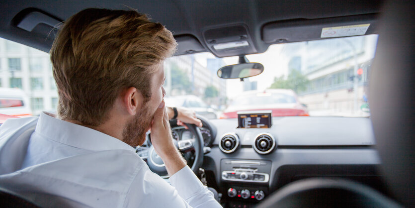 Ein Mann sitzt im Auto. Durch die Windschutzscheibe sieht man einen Stau vor ihm