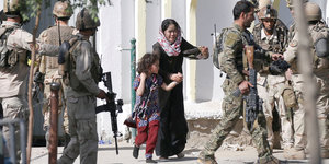 Eine Mutter rennt mit ihrer kleinen Tocher in heller Panik, um sie herum stehen Soldaten