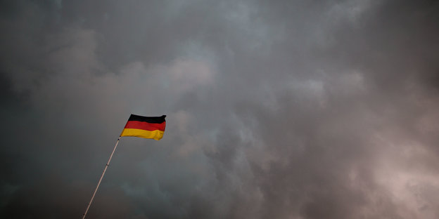 Eine Deutschlandfahne vor dunklen Wolken